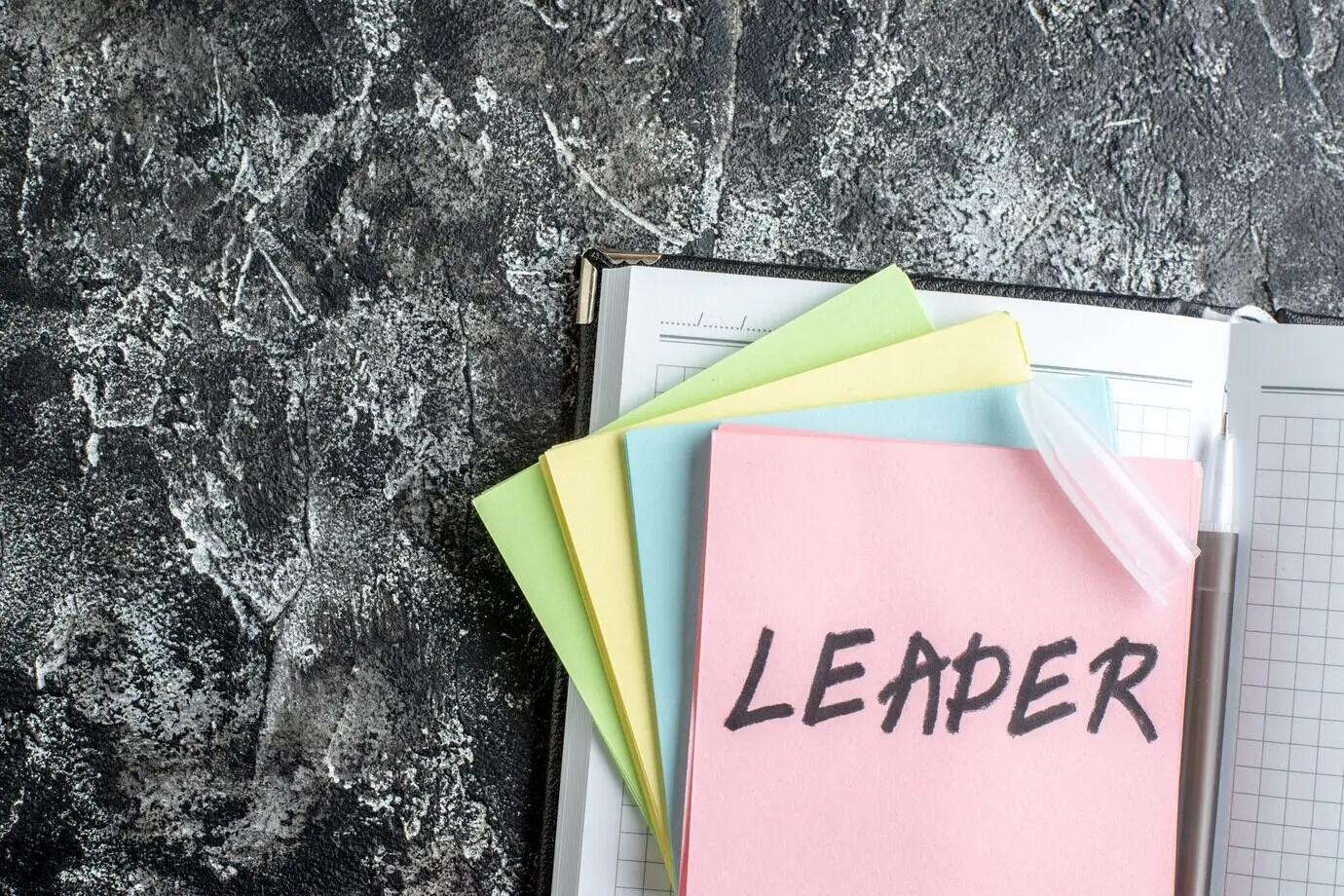 Вид сверху на записку с надписью «leader», стикеры и тетрадь на сером фоне.